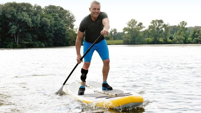 Henning riding a standup paddleboard while wearing a WalkOn brace