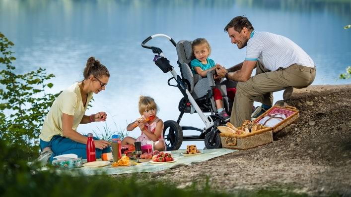 Emilia in ihrem Ottobock Kimba Rehakinderwagen beim Picknick am See mit Familie.