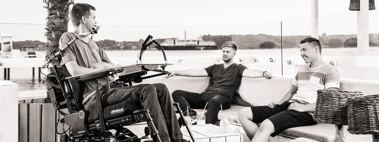 Ottobock’s Juvo power wheelchair – scene: a wheelchair user and two friends on a dock near the water