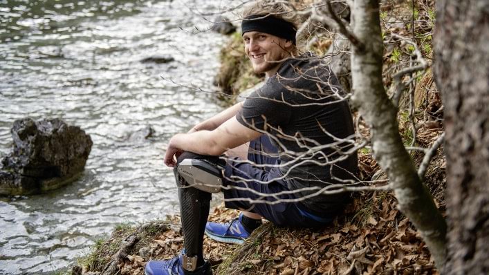David wears a C-Brace orthotronic mobility system. He is smiling at the viewer while sitting by a lake.