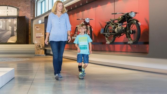 Mutter und Sohn gehen durch eine Motorrad-Ausstellung. Der Junge trägt die WalkOn Reaction junior, eine dynamische Unterschenkelorthese von Ottobock
