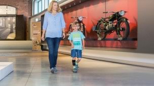 Madre e hijo visitando una exposición de motocicletas.  El niño lleva puesto el WalkOn Reaction junior, una ortesis dinámica de tobillo-pie de Ottobock