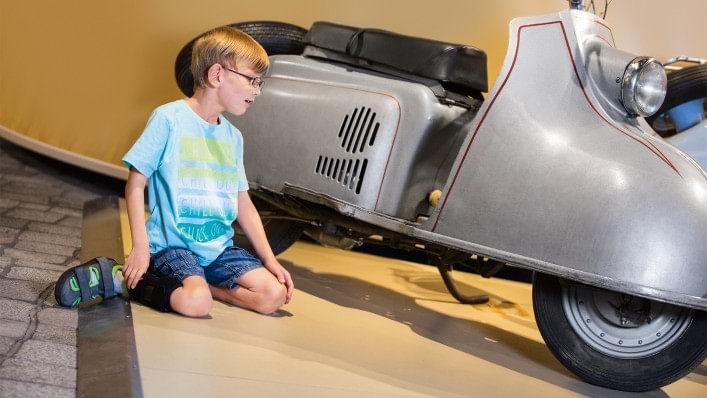Boy looking at a scooter. He is wearing the WalkOn Reaction junior, a dynamic ankle-foot orthosis from Ottobock