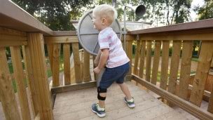 Niño jugando en un patio de recreo.  Lleva la WalkOn Reaction junior, una ortesis dinámica de tobillo-pie de Ottobock, en su pierna izquierda