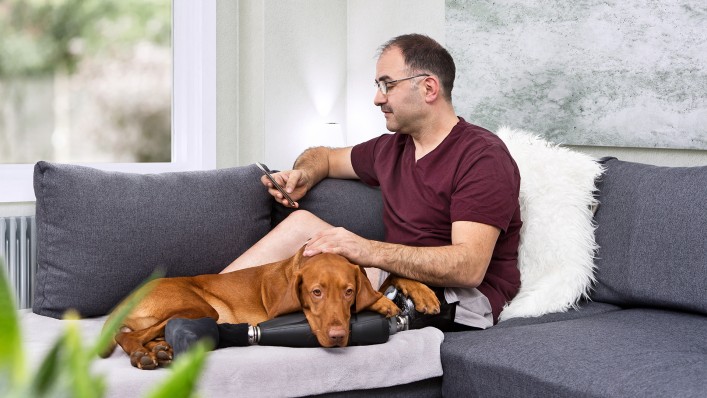 Feri rests on the sofa with his dog Kari lying on his prosthesis.