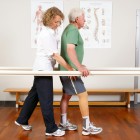 A physiotherapist conducts gait exercises at the parallel bars with a prosthesis wearer.