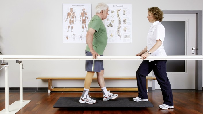 The therapist performs a balance exercise at the parallel bars with a prosthesis wearer.