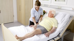 A therapist is standing at the hospital bed of a leg amputee, massaging his residual limb.