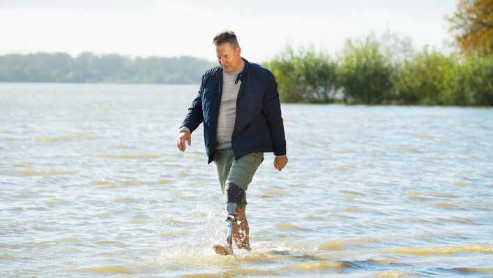 User of the Quickchange adapter for changing prosthetic feet walking in the water along a riverbank.