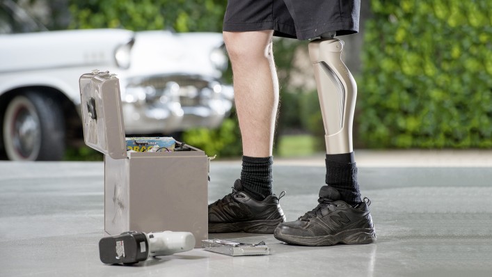 Man’s legs in front of a toolbox; he is standing with his legs hip-width apart and one knee slightly bent. He wears a C-Leg on his left leg.