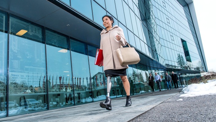 A user with the C-Leg leg prosthesis walking to work outside a glass-fronted office building.