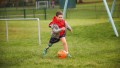 Kleiner Junge spielt Fußball auf Rasen – dabei streckt er sein Prothesenbein zu einem großen Ausfallschritt.