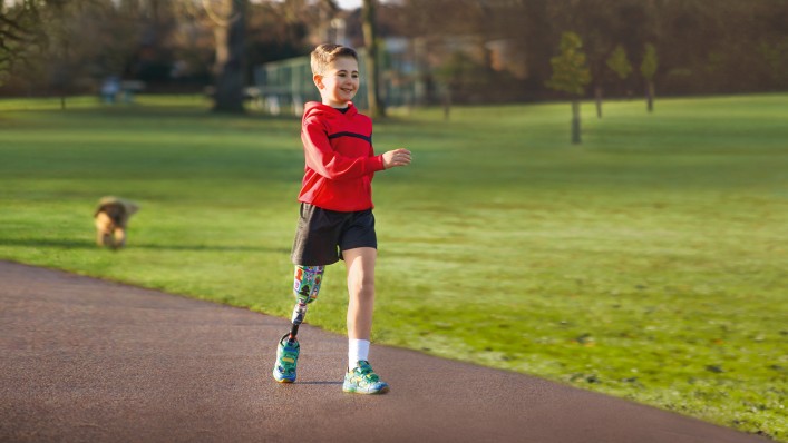 A young boy takes a running step on the footpath in the midst of a park.