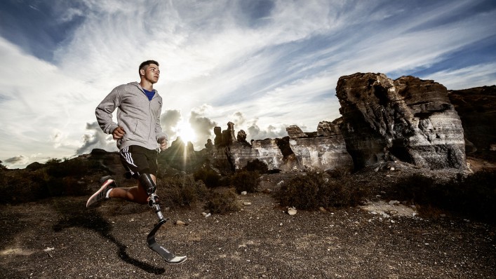 Uživatel sportovní protézy běží členitým terenem.