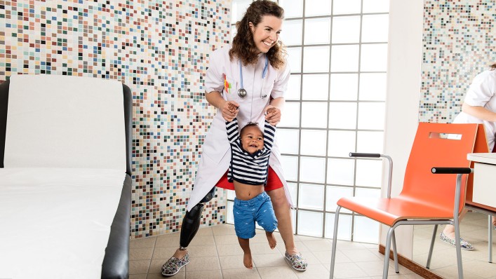 Marije playfully swings a young patient around by her hands in a treatment room. 