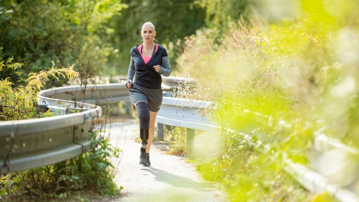 Junge Frau, die eine Prothese mit der aktiven Vakuumpumpe DVS (Dynamic Vacuum System) trägt, joggt im Freien