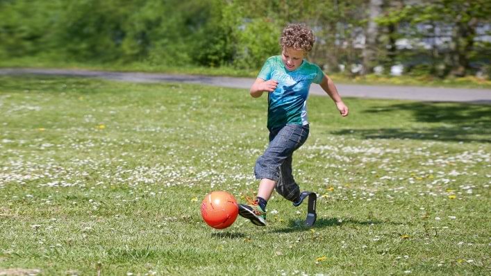 Bambino che gioca a calcio nel prato con una protesi da sport