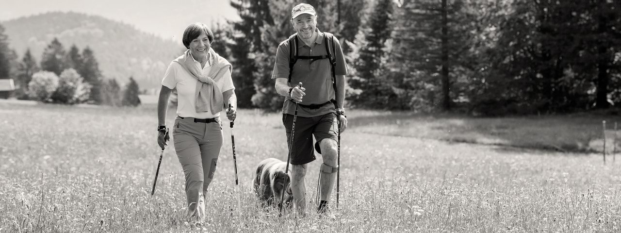 Arthrose Betroffener mit Agilium Freestep wandert mit Frau und Hund über eine grüne Wiese