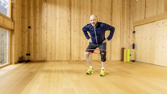 Arthrose Betroffener mit Agilium Move führt Kraftübungen für die Beine mit Gummiband aus.