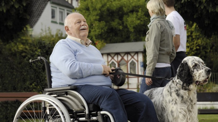 Une homme âgé en fauteuil roulant, en promenade avec son chien