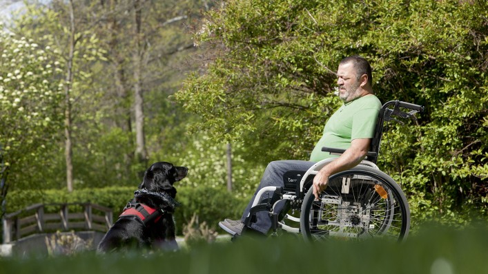 Un homme en fauteuil roulant, en promenade avec son chien