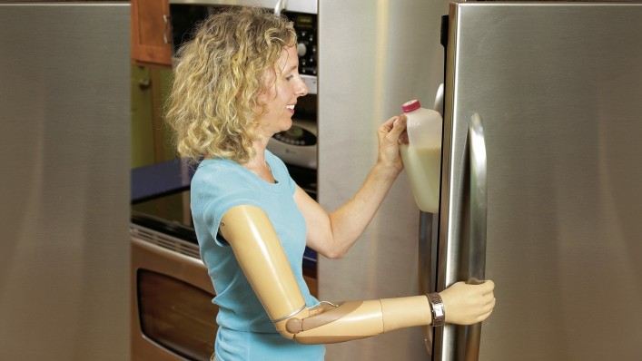 Sherri with DynamicArm prosthesis opening the door of the refrigerator to put a milk bottle back.